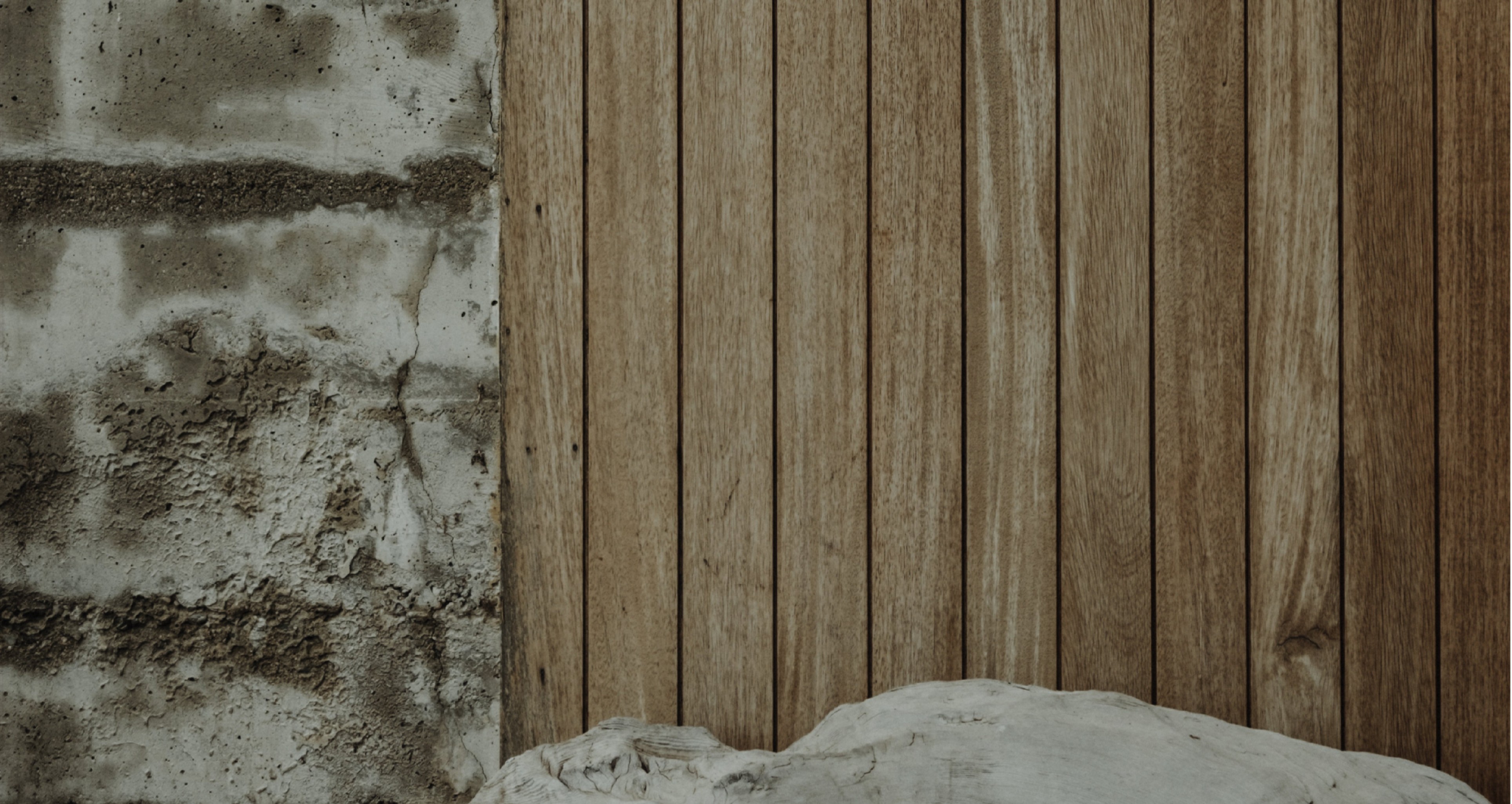 Rough concrete wall next to vertical wooden planks with a weathered driftwood log at the base.