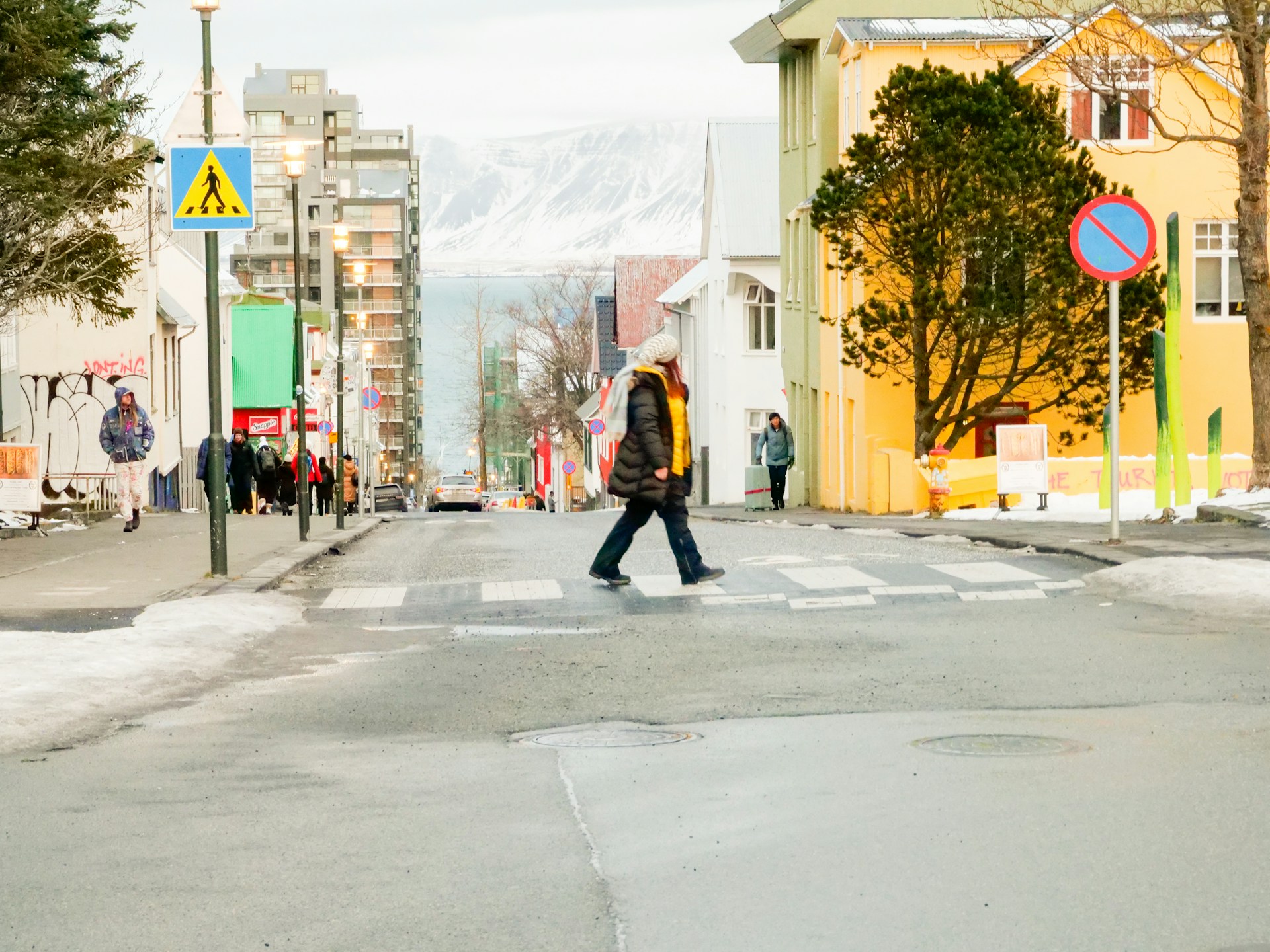 Pedestrian crossing a street in downtown Reykjavík with colorful buildings and mountains in the background.