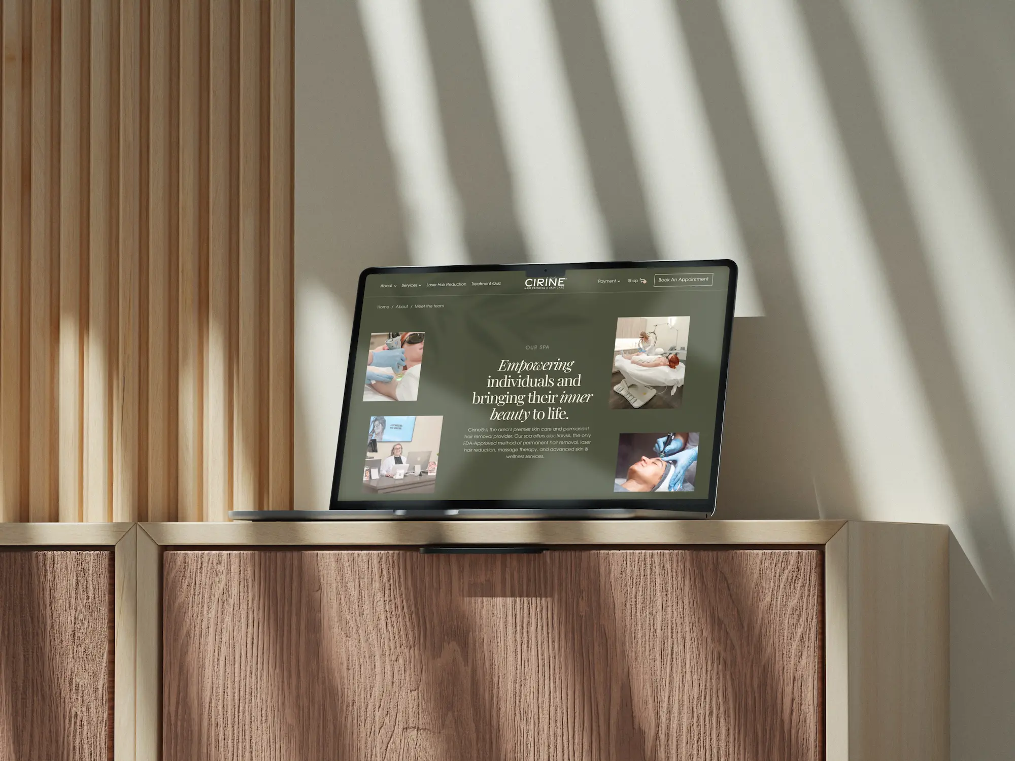 A sleek laptop sits on a wooden surface, illuminated by soft shadows from nearby blinds.