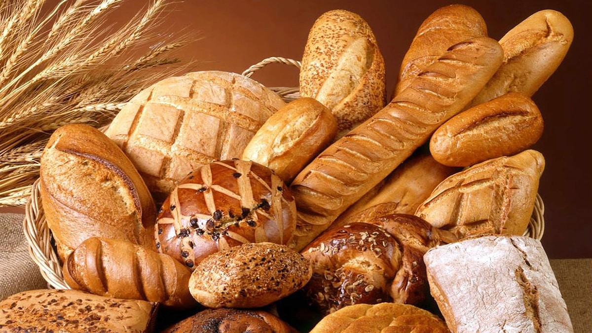 A basket filled with an assortment of wheat breads, rolls, and baked goods that contain gluten