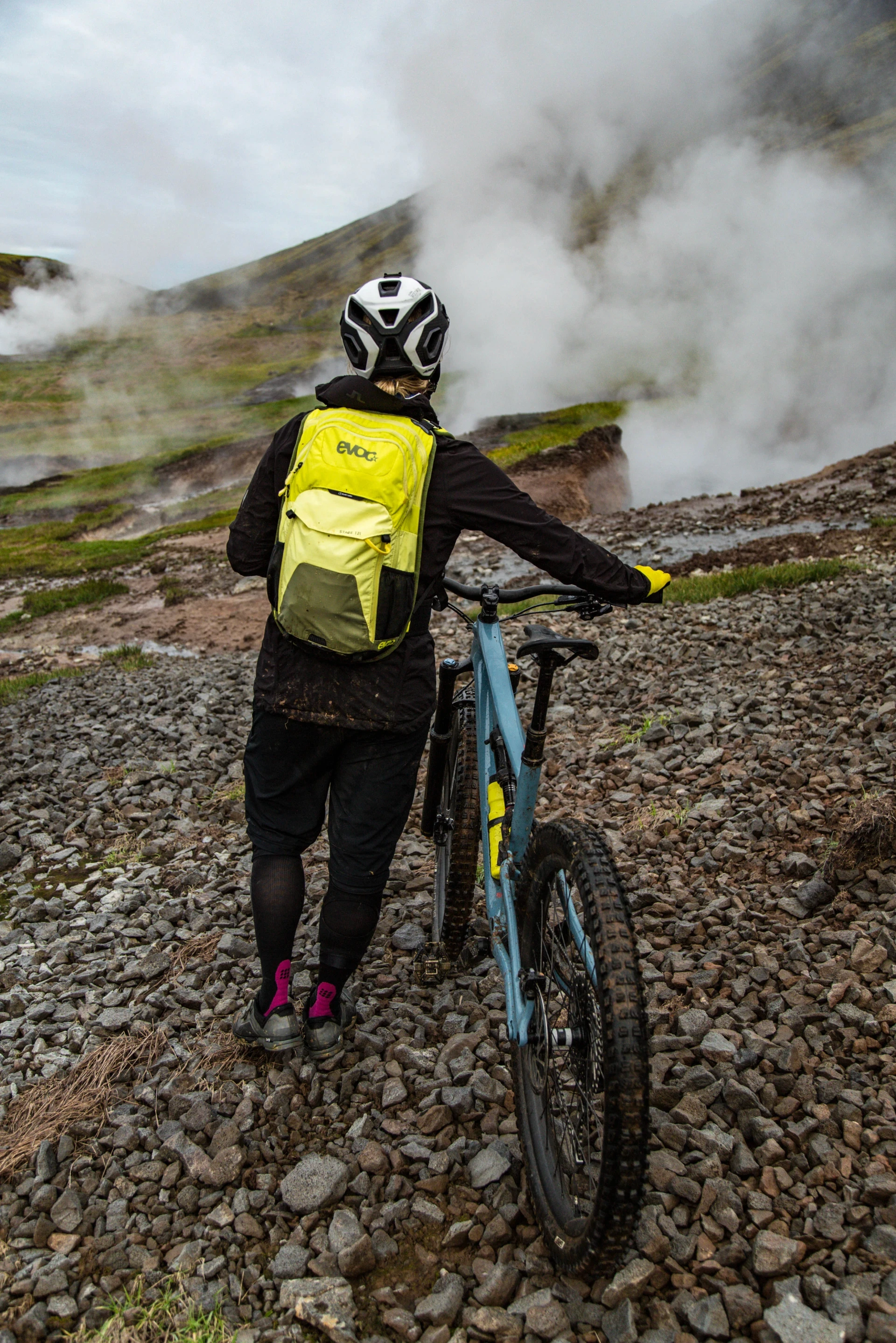 Woman with evoc backpack walking away from camera with her bike in Iceland