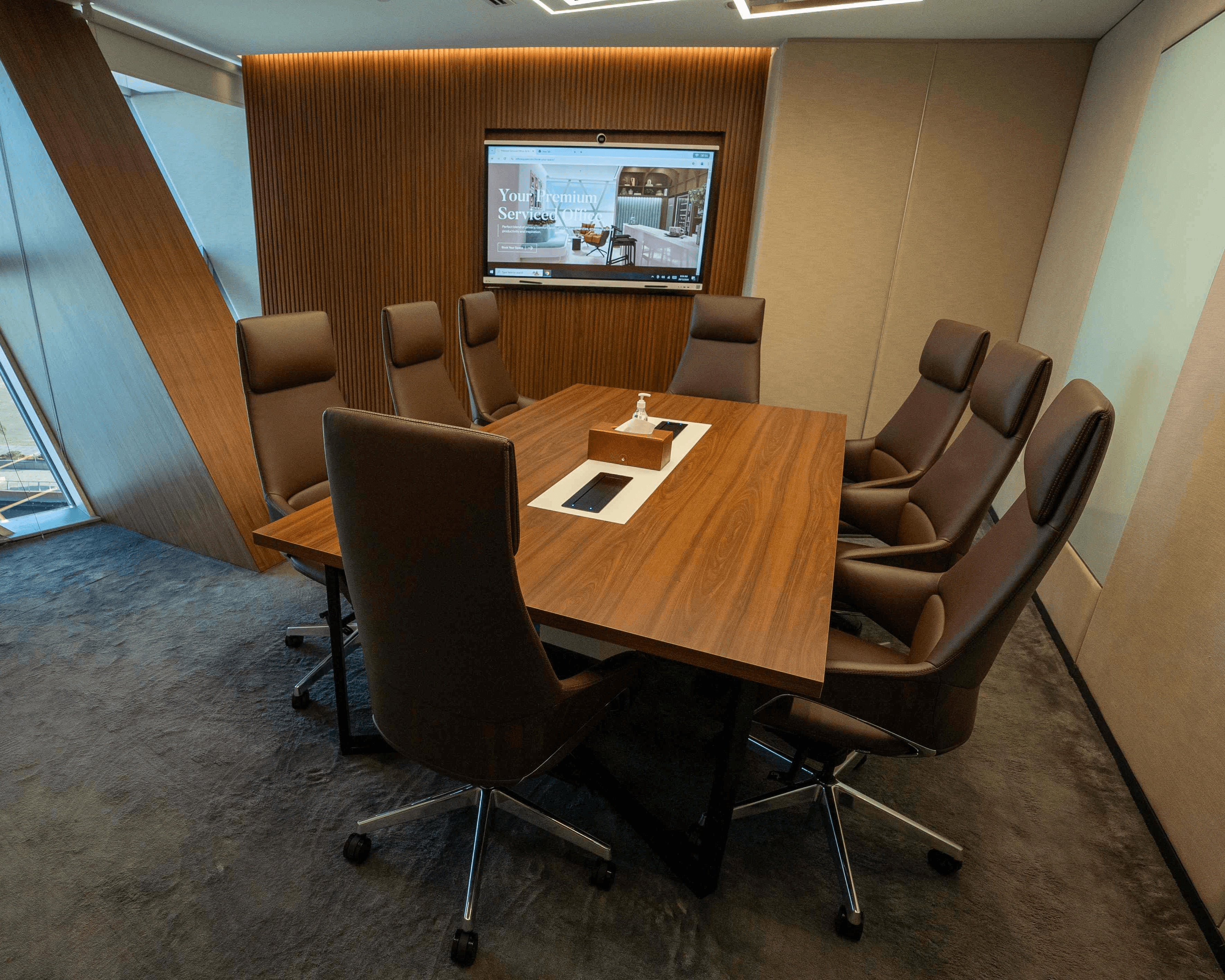 Premium meeting room in Dubai featuring a wood-paneled wall, high-definition screen, and an 8-seater conference table.