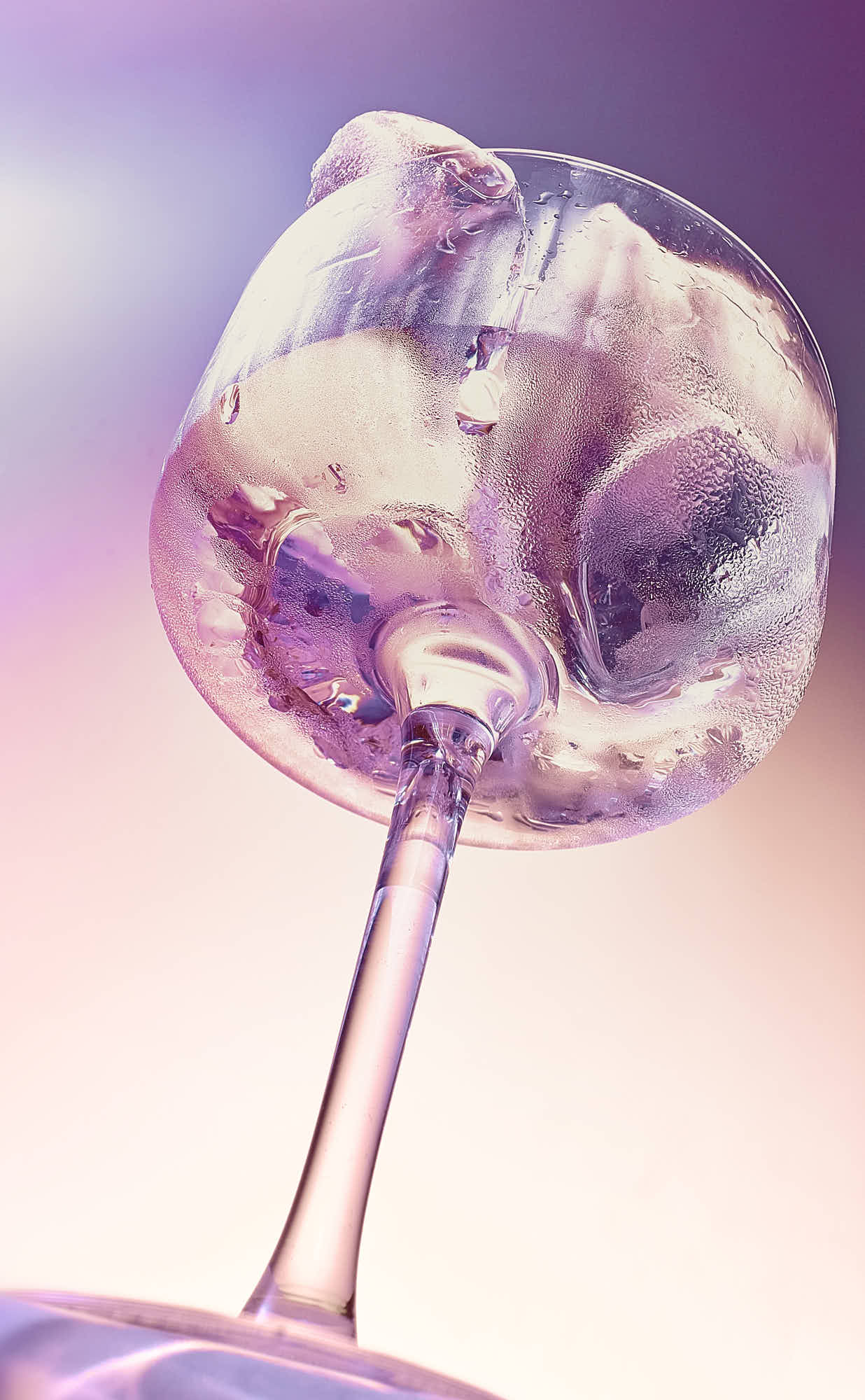 A wine glass with ice cubes in with a swirled colorful design, set against a soft pastel background.