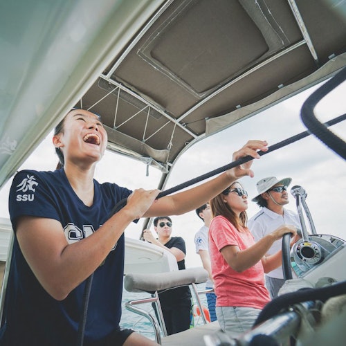 一群人在船上航行。一人一边处理绳子一边笑，其他人站在旁边，微笑并享受航程的乐趣。