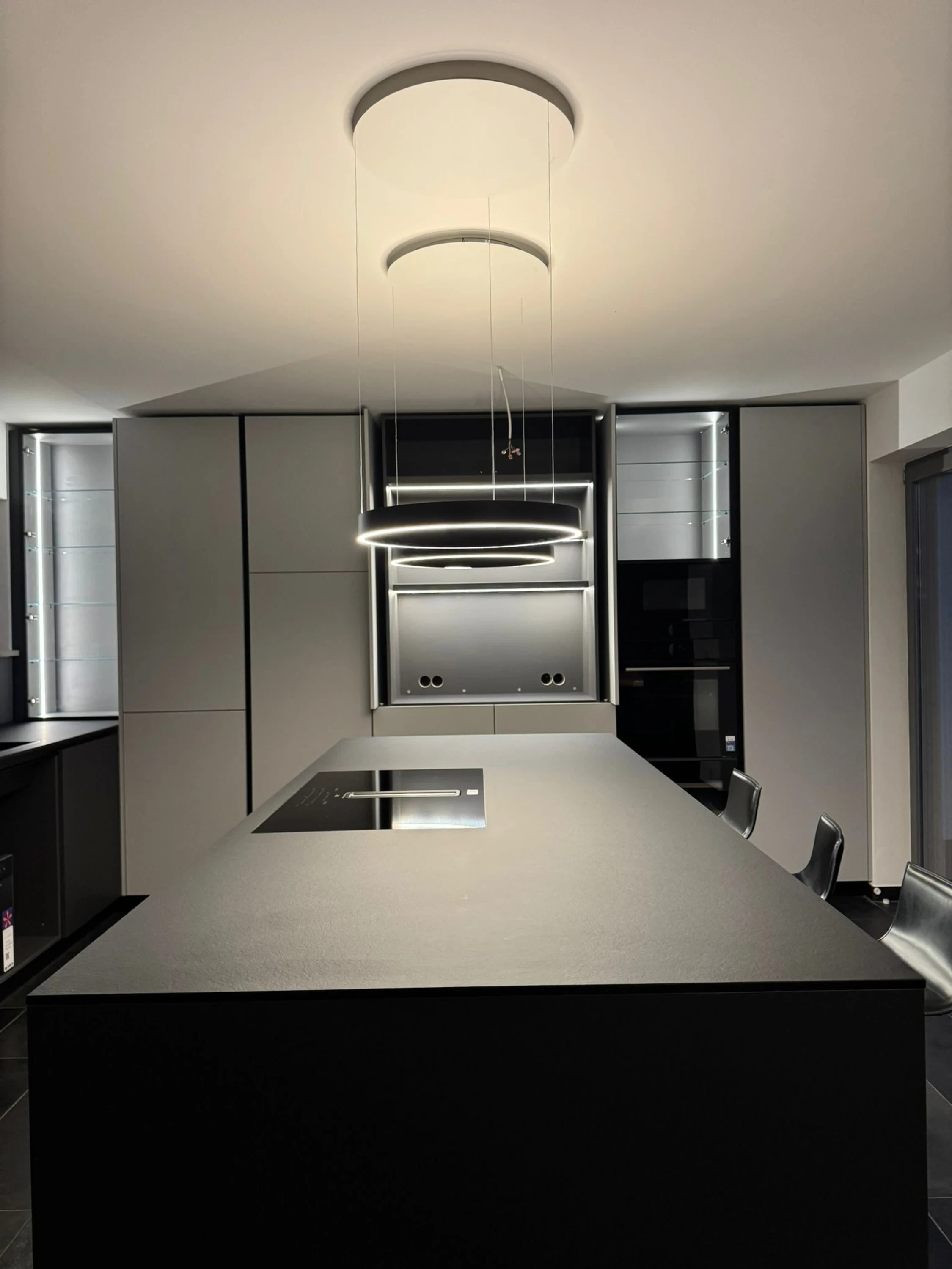 Salon-cuisine ouvert rénové au Luxembourg : canapé modulable, parquet chêne, cuisine encastrée gris mat, éclairage LED linéaire.