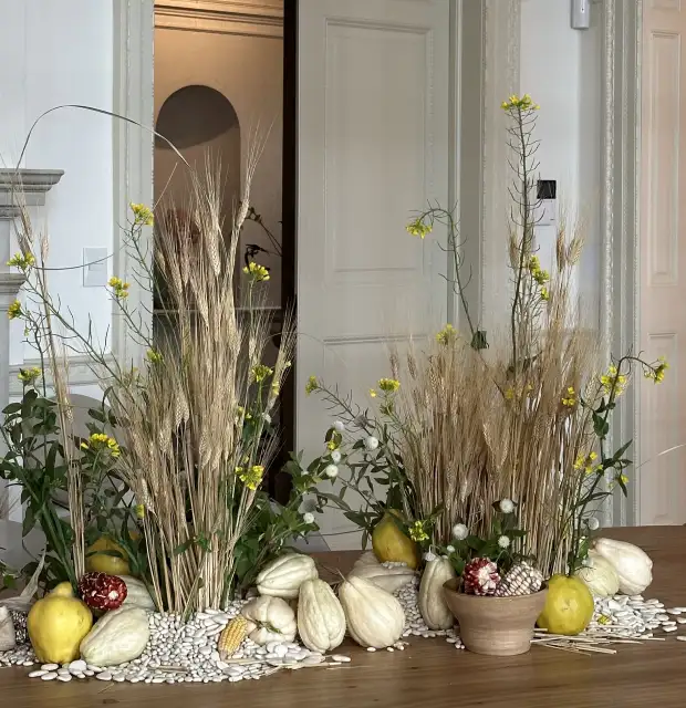 Composición otoñal con espigas, flores amarillas y calabazas decorativas para ambientación natural en interior clásico.