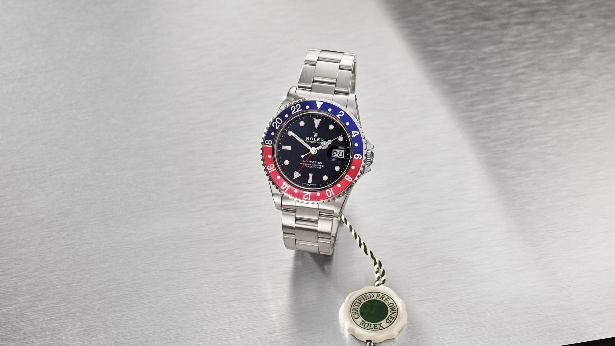 Luxury Rolex GMT-Master II watch with blue and red bezel on a stainless steel bracelet displayed on a metallic surface.