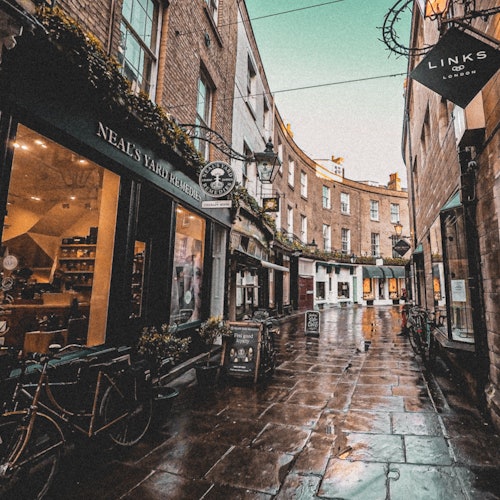 一条狭窄而湿滑的鹅卵石街道,街道两旁是商店和自行车,在都市环境中可以找到Neal’s Yard Remedies和Links。