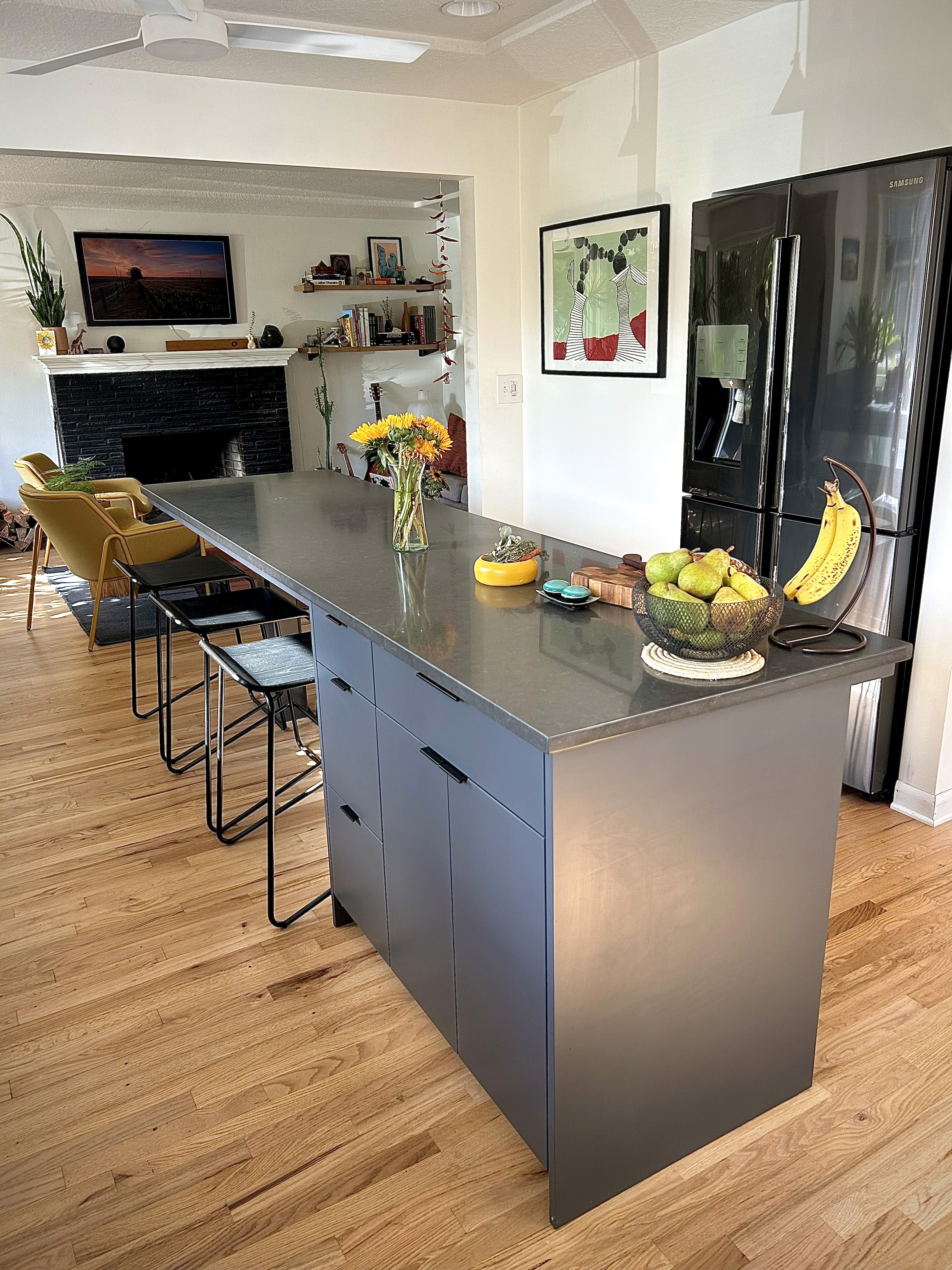 A black long black kitchen island holds colorful fruits and flowers with stools tucked underneath.