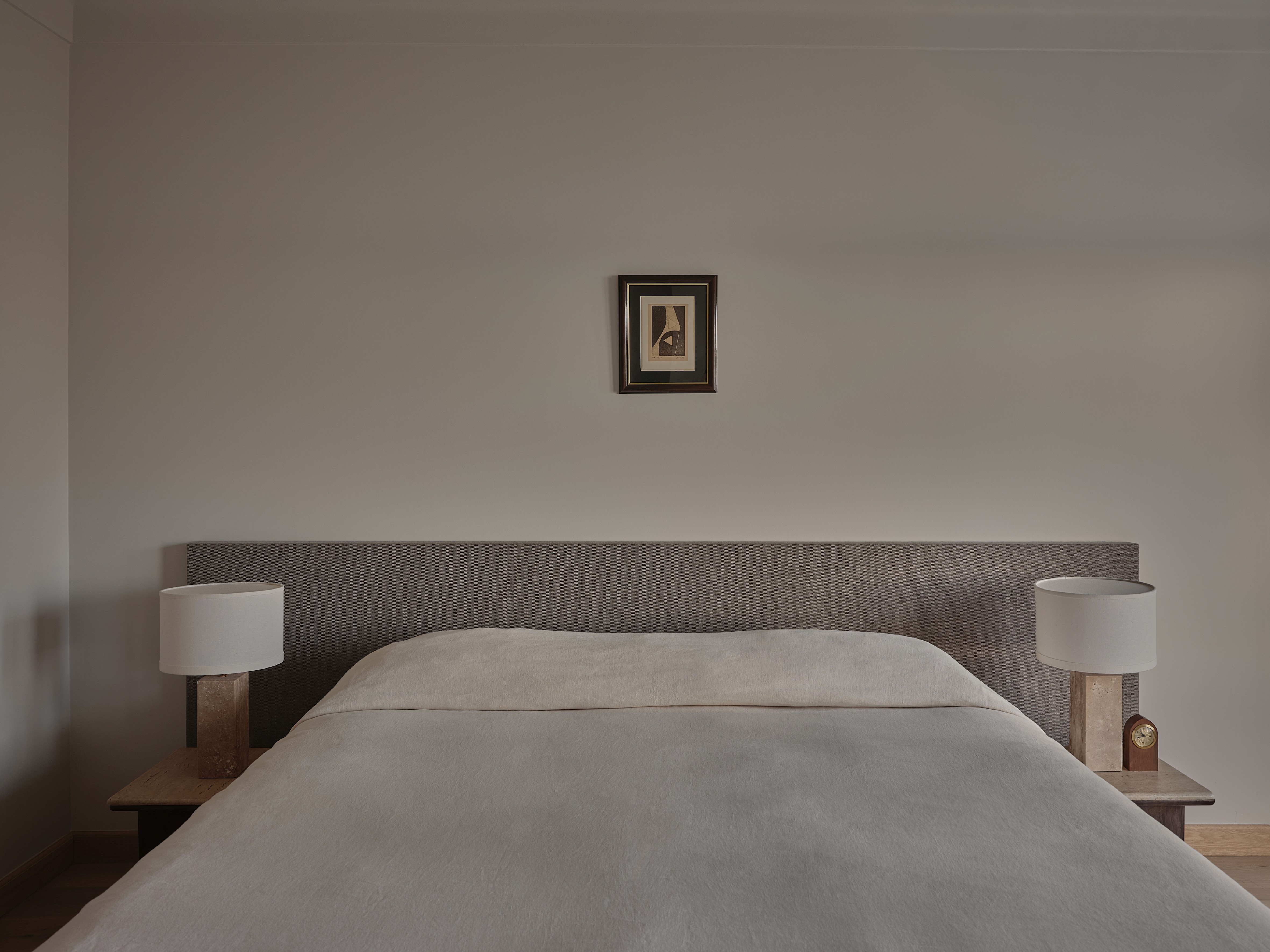 Master bedroom with upholstered linen headboard, white ceramic table lamps, and vintage artwork above bed