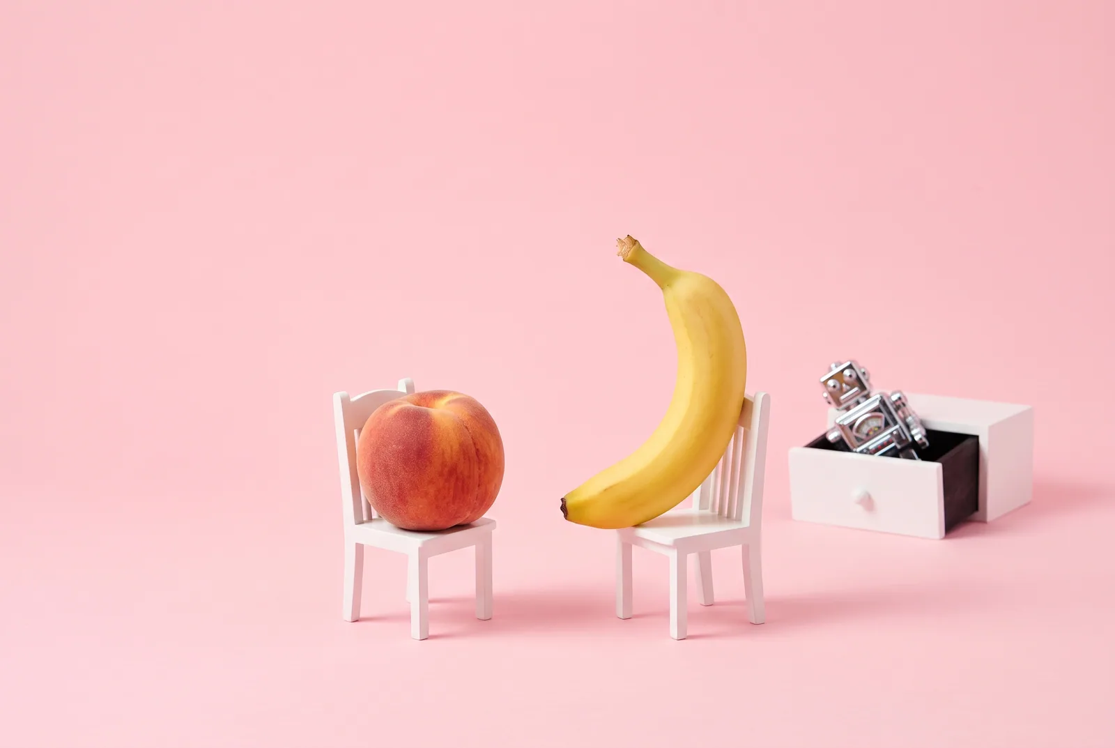 A peach and a banana face to face with a chrome robot put away in a drawer, talking it through: is it cheating if it's AI