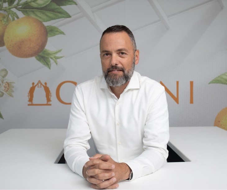 Photo of Dan Mora, the founder of Gemini Legal in front of the Gemini logo. He is sitting  behind a white desk in a white collared shirt with his arms resting on the desk and hands clasped in front of him. Wearing a pensive expression. 