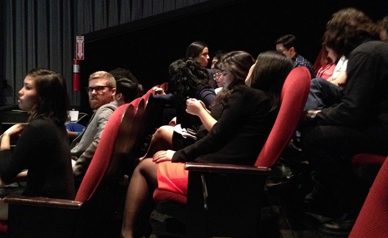 A photo of some people sitting in a theatre and watching the show.