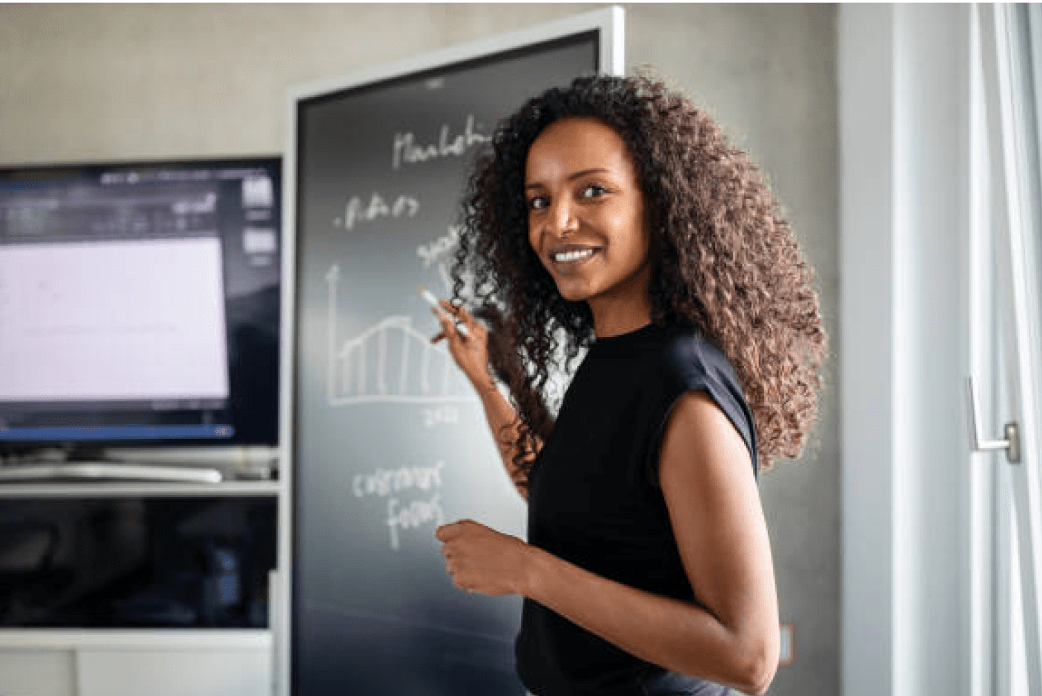 A lady teaching with a black board behind her