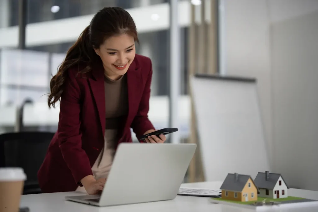 Accounting for rental property being managed by a real estate agent using a smartphone and laptop in office.