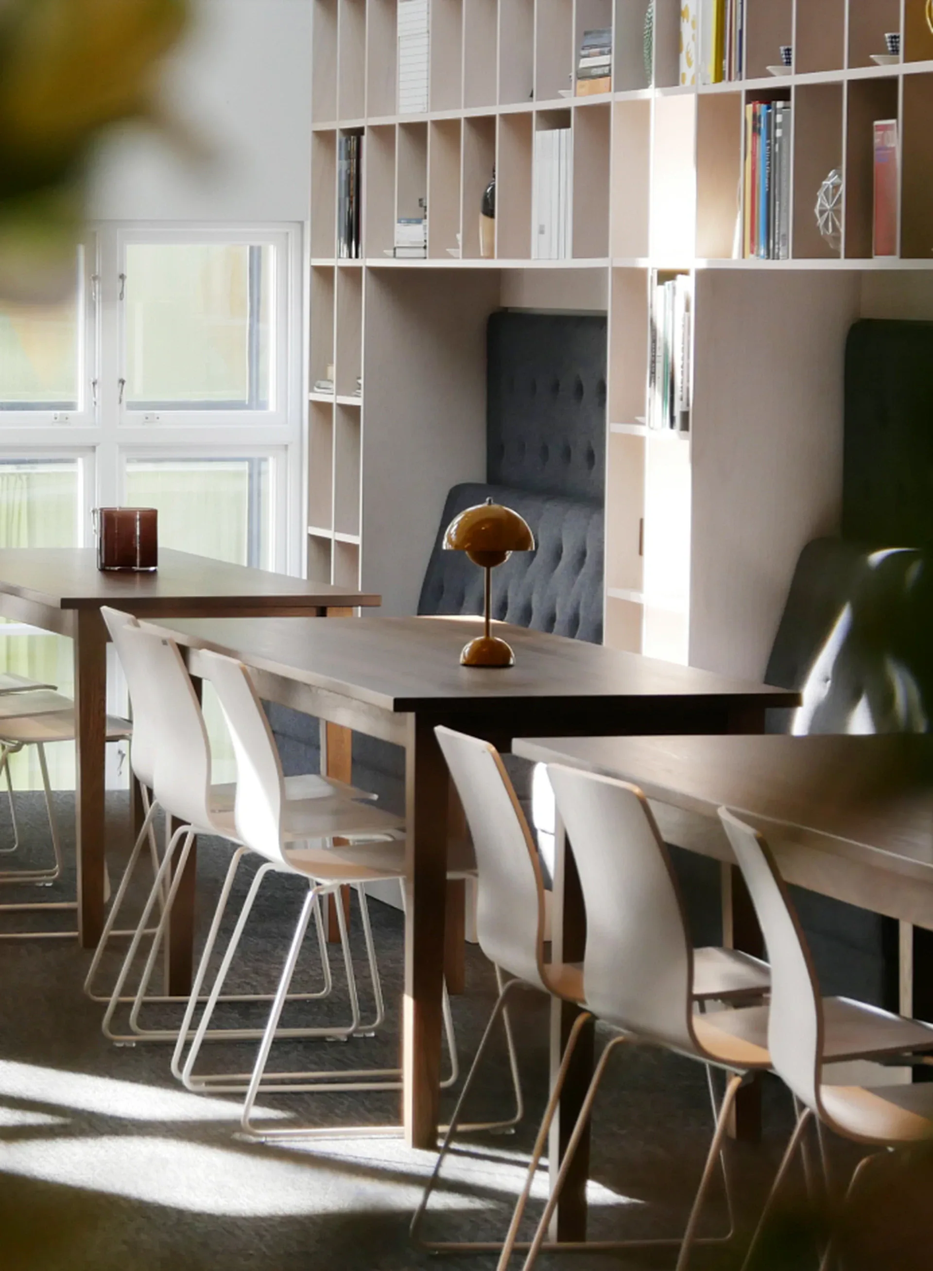 Kontor med långbord, vita stolar och en bokhylla i solljus