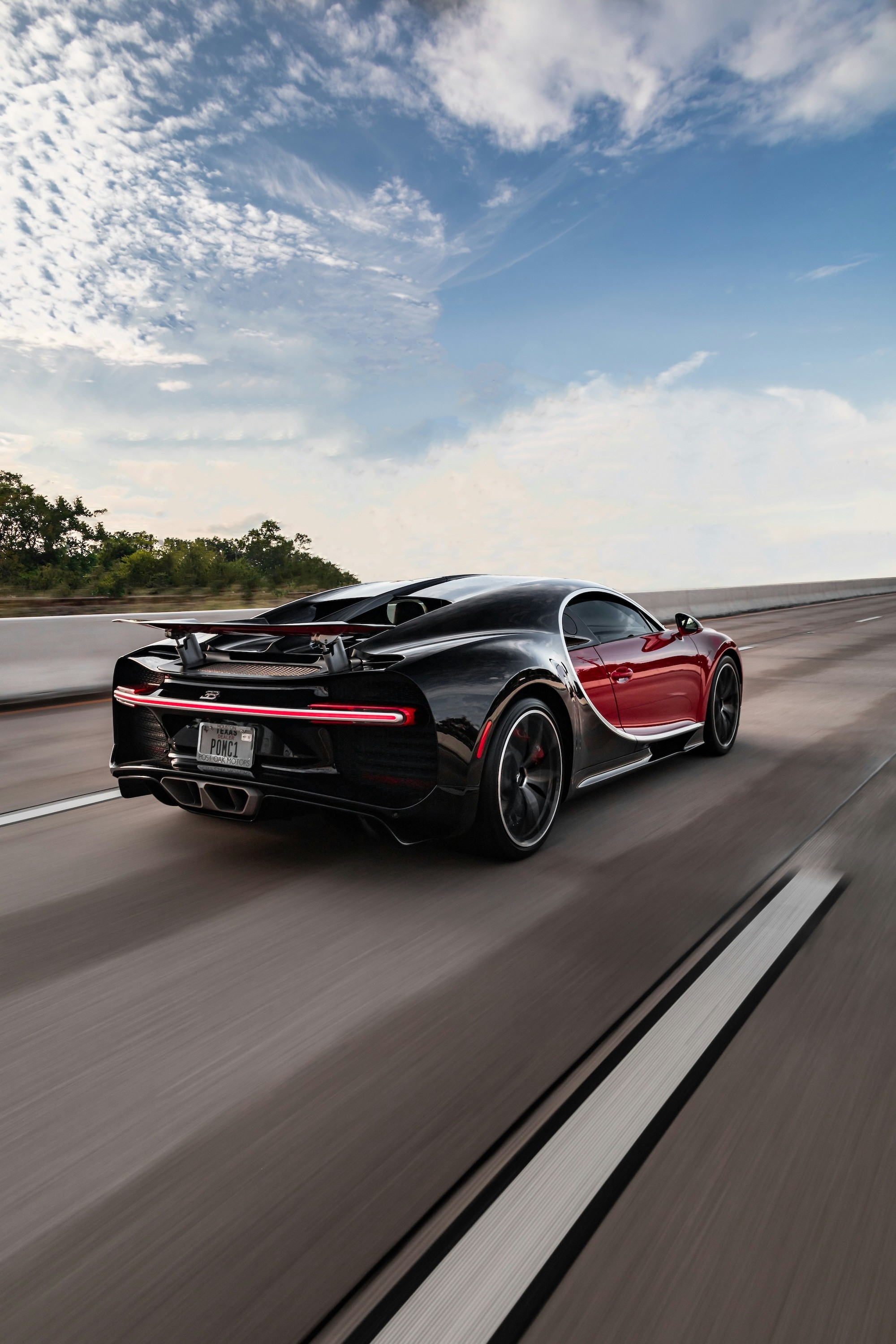A sleek, black and red sports car speeds down an open highway under a clear, blue sky, symbolizing freedom and luxury automotive performance.