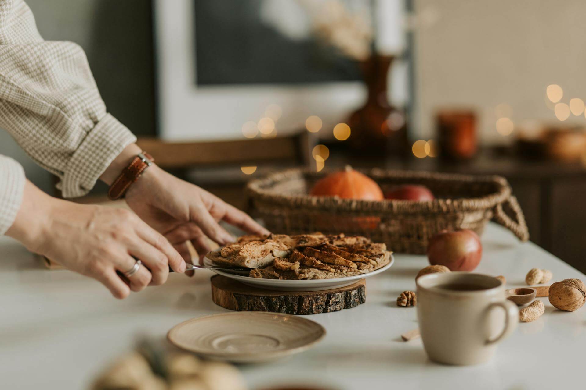 A person slices a pie on a table, showcasing the dessert's filling and crust in a cozy setting