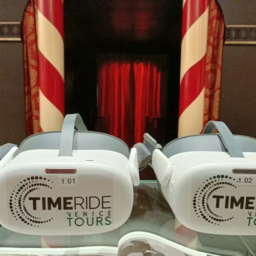 Due visori per la realtà virtuale con la scritta 'TimeRide Venice Tours' su una superficie riflettente, con uno sfondo in stile teatrale.