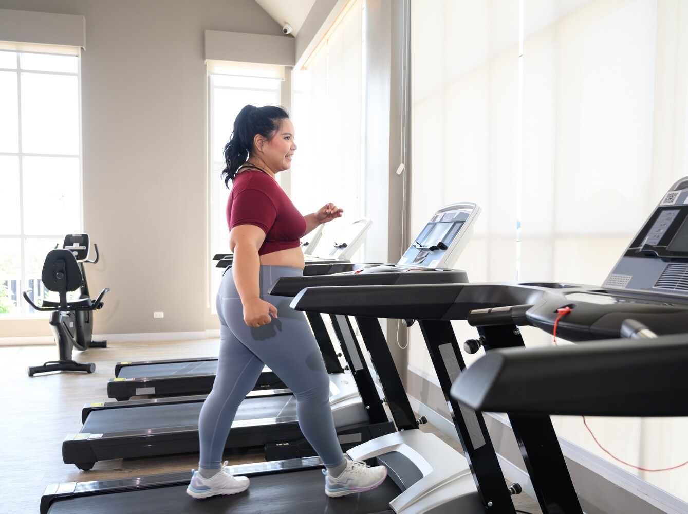 plus-sized woman walking on a treadmill to lose weight at the gym and smiling as she enjoys herself