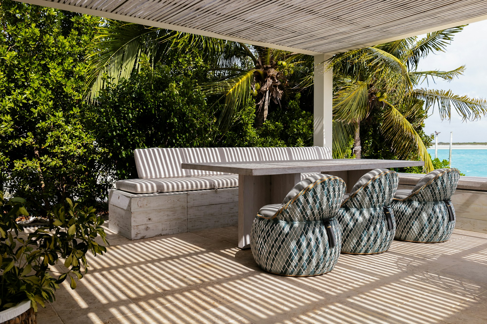 Shaded garden terrace with a stone dining table, striped bench and palms beyond
