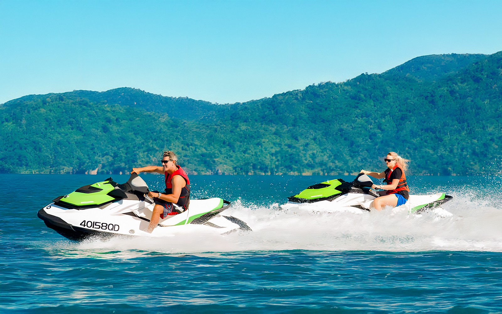 תיירים רוכבים על אופנועי ים באיי וויטסנדיי עם גבעות ירוקות ופוריות ברקע.