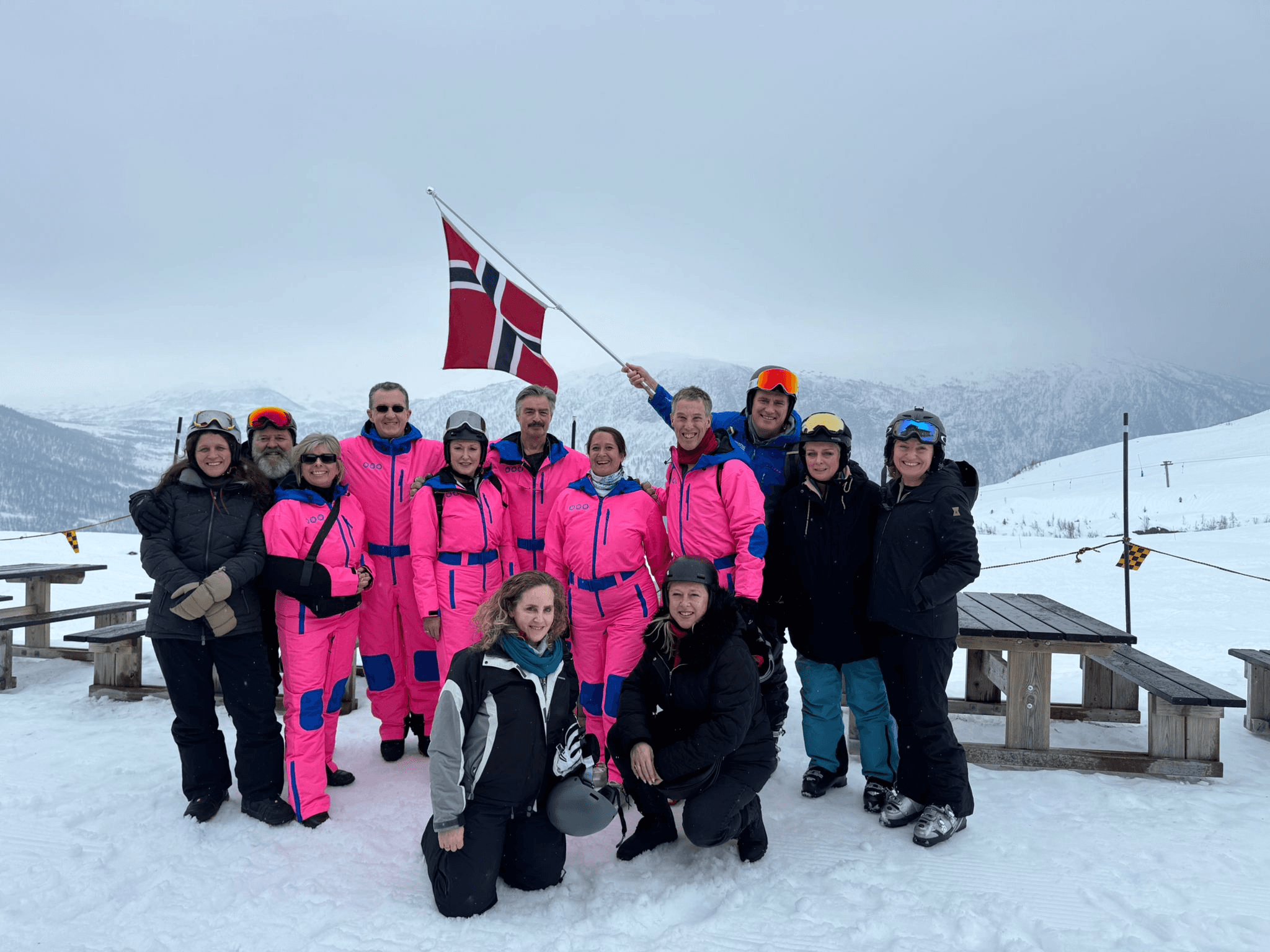 Cozy reading nook with sofa, chair, and plants inside a glass cabin with mountain forest views.