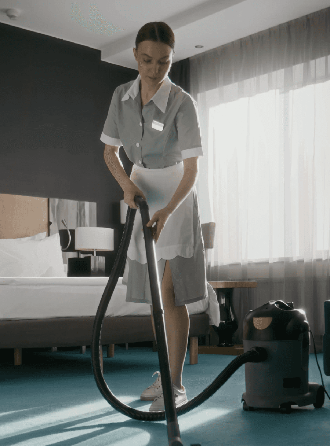 a woman in a green shirt and black gloves vacuuming a gray ottoman