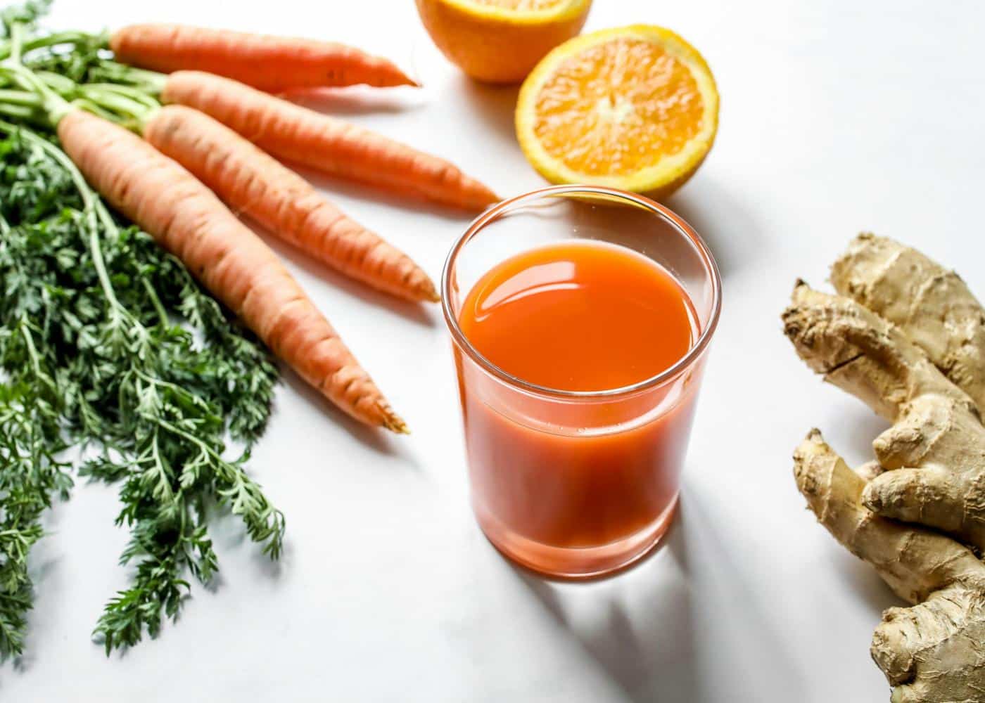 Orange juice in glass next to a bunch of carrots, oranges and ginger