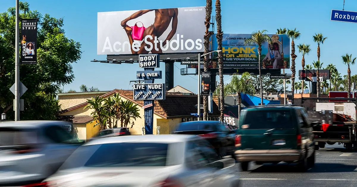 a man walking down a street past a large poster