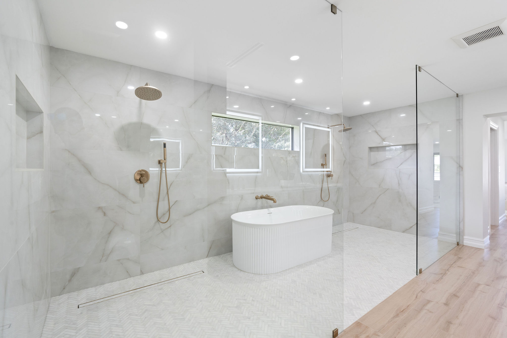 Modern bathroom with white marble, freestanding tub, and glass shower stalls.