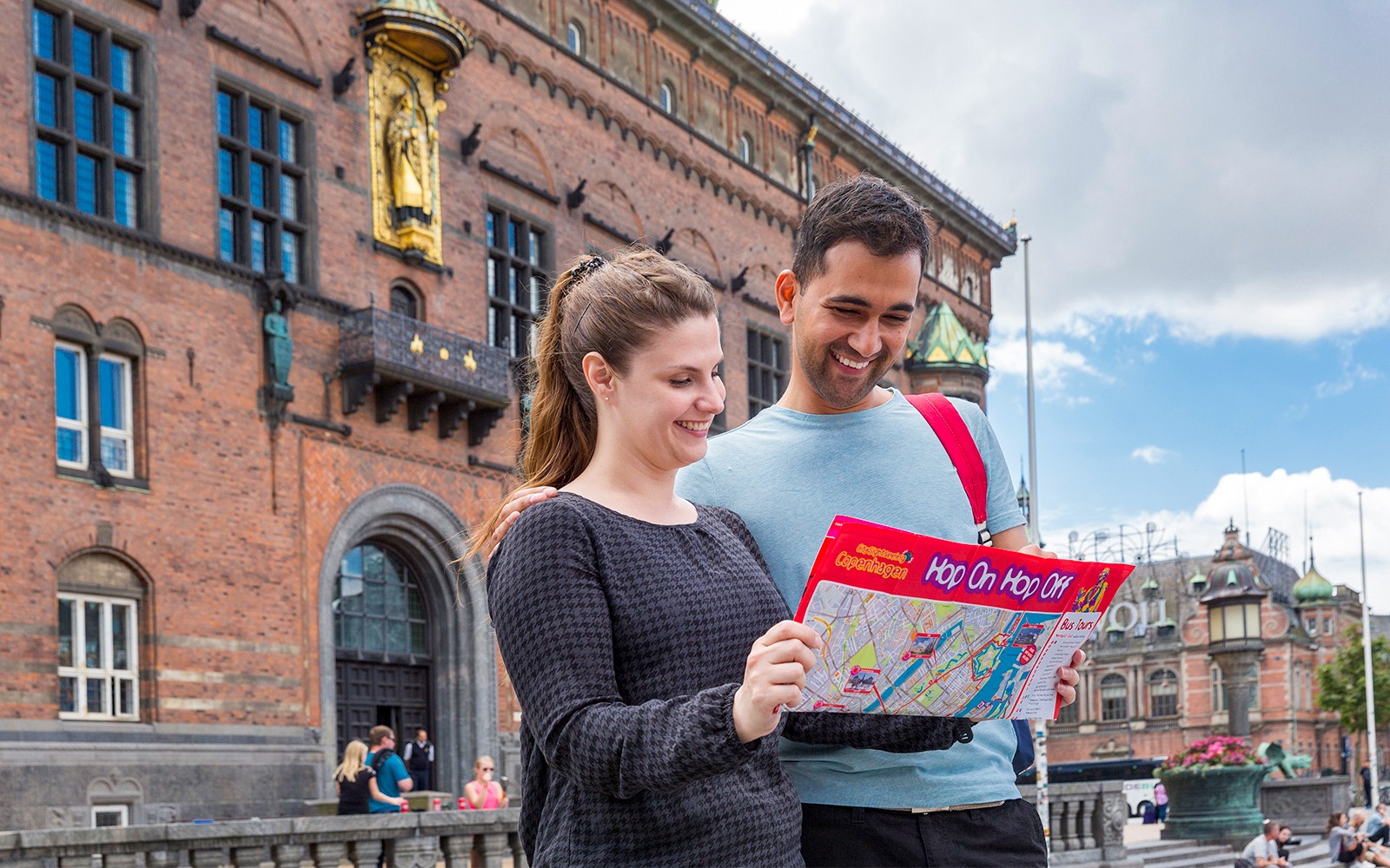 Barátok vizsgálják a koppenhágai HOHO busz útvonaltervét egy történelmi épület közelében.