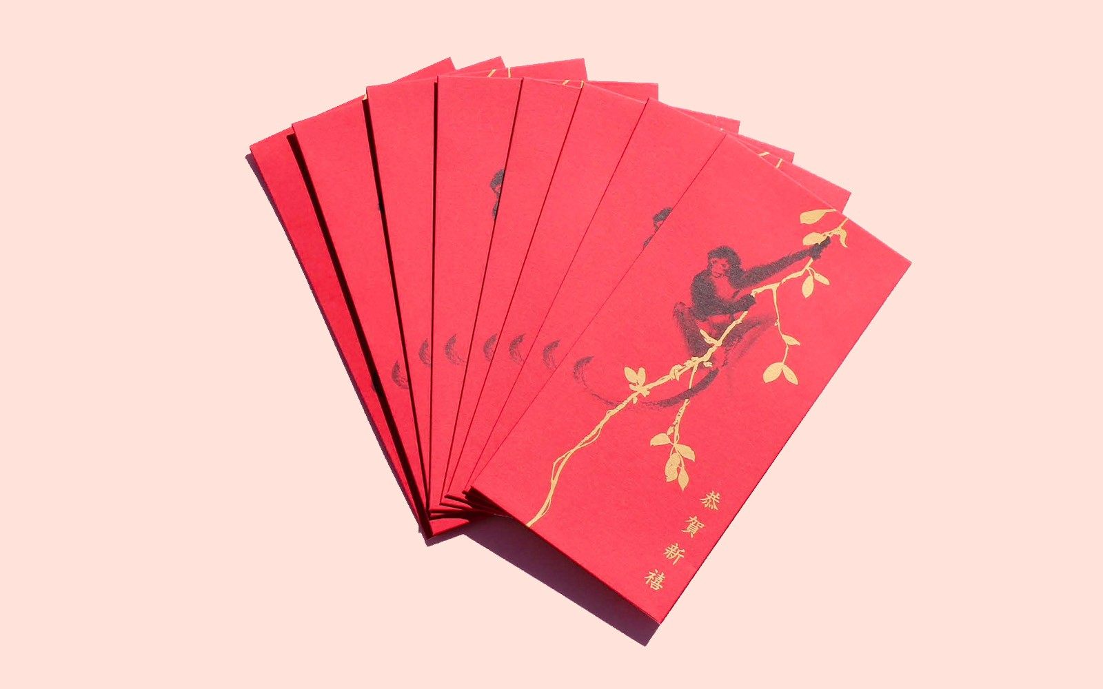 Red envelope with a black monkey hanging off a foiled gold branch. Happy New Year in madarin in the bottom left hand corner