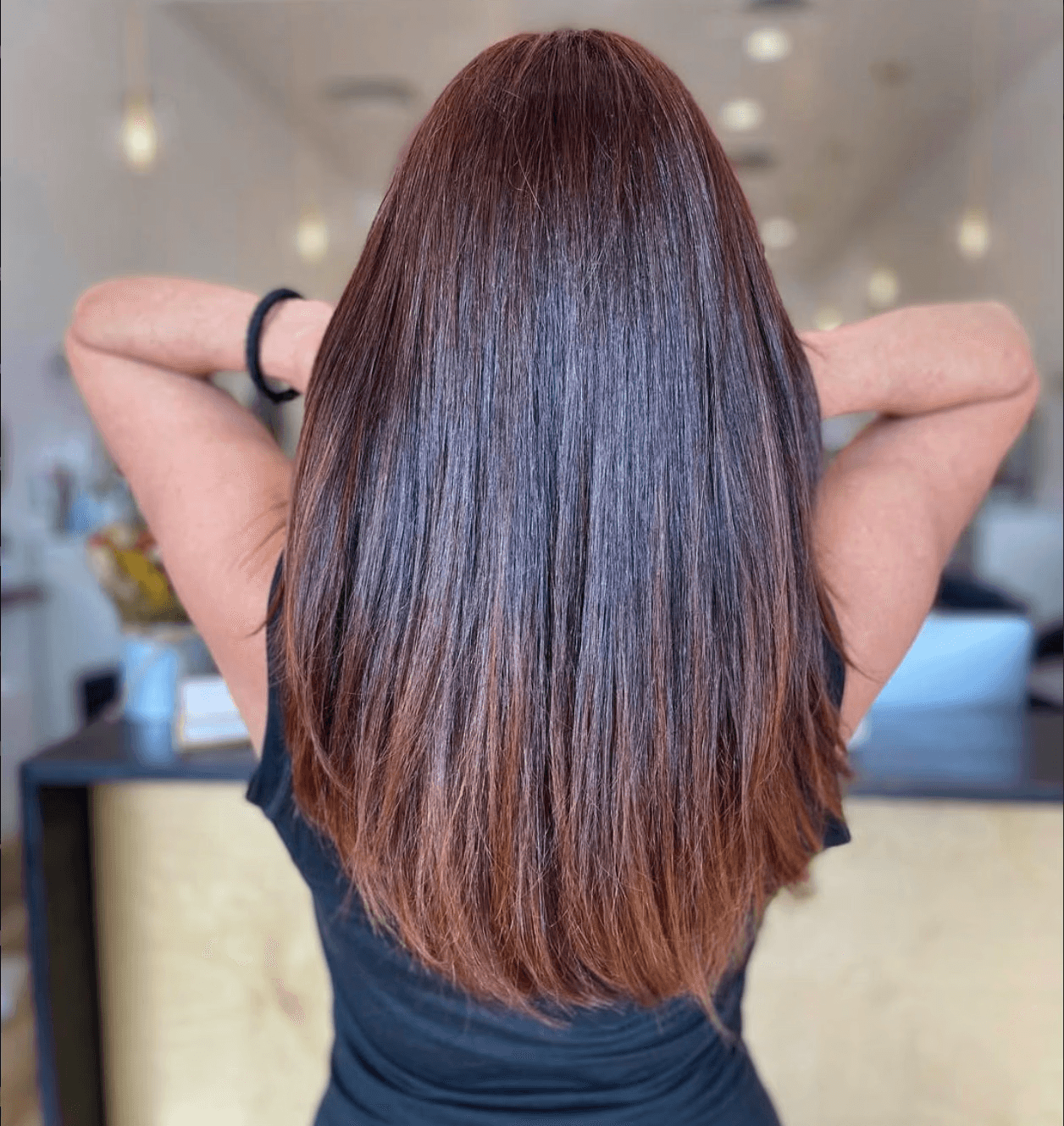 Back view of long, straight brunette hair with a rich auburn ombré, styled smooth and glossy for a glass-hair finish.