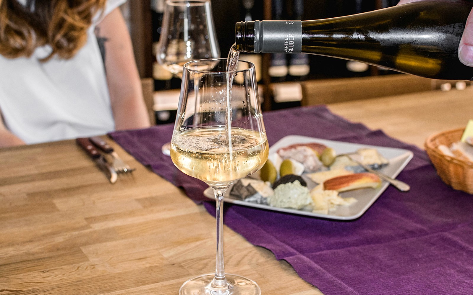 Vin hældes i et glas på en skjult vinbar med et ostefad i nærheden.