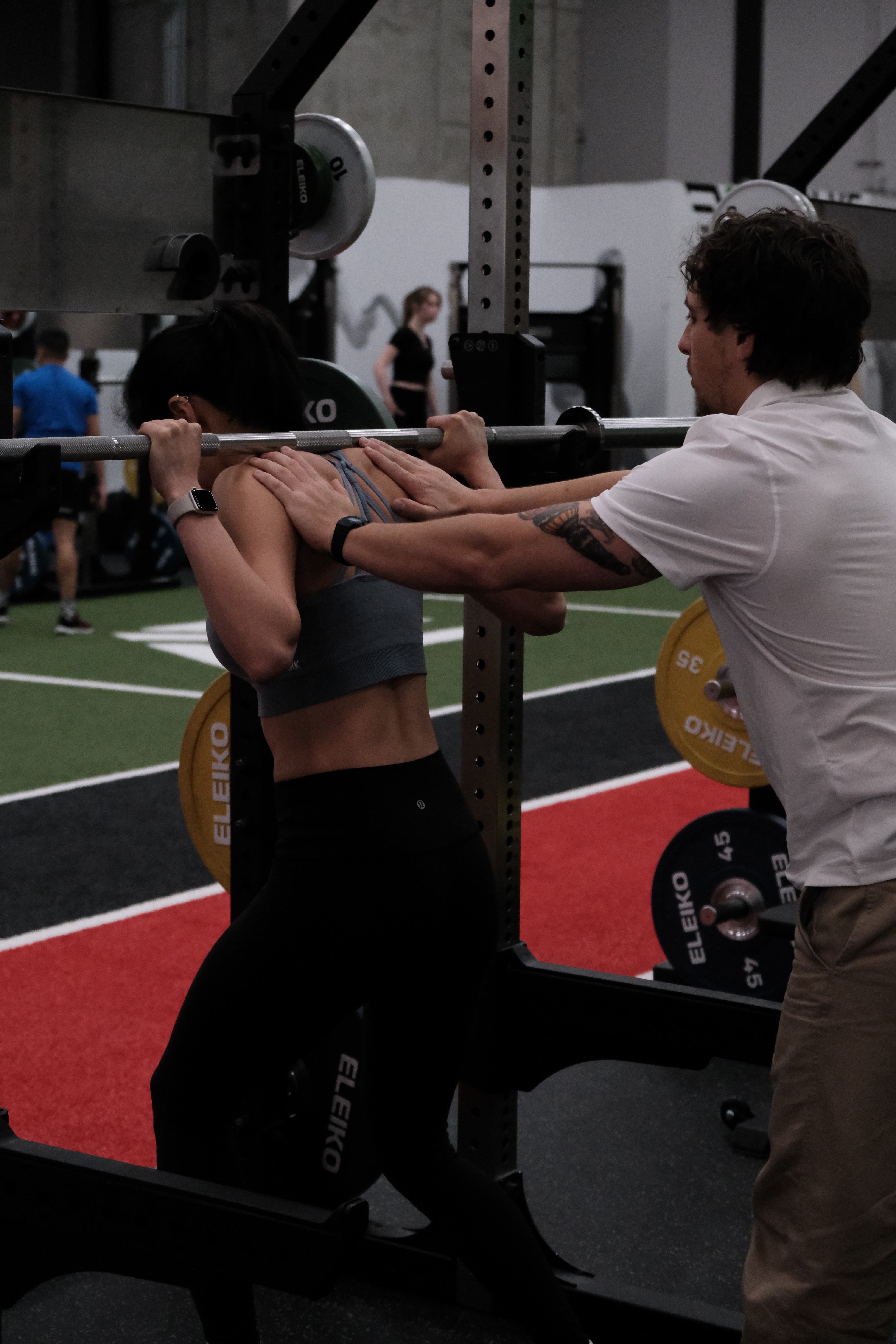 physiotherapist spotting a patient performing a barbell back squat