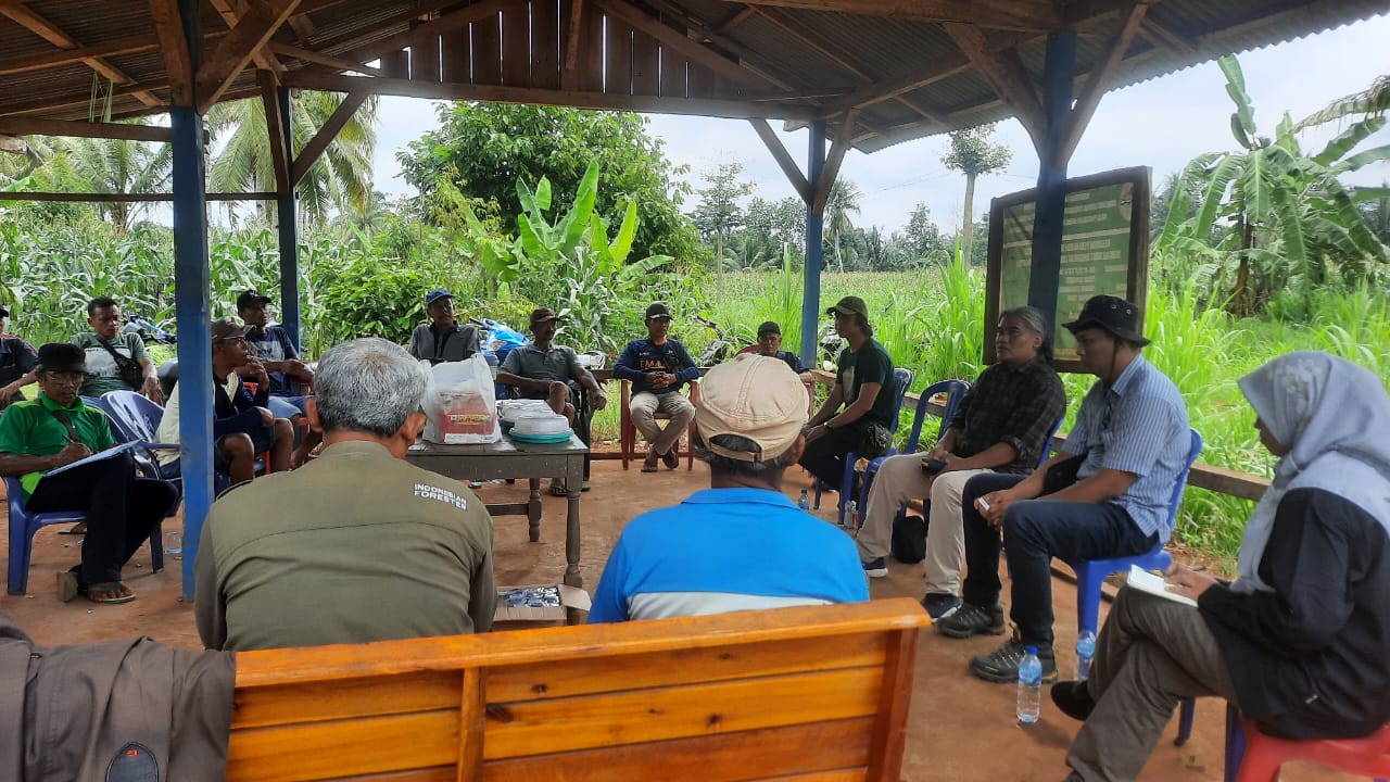 A group of people seated in a gazebo, engaged in discussion surrounded by greenery.