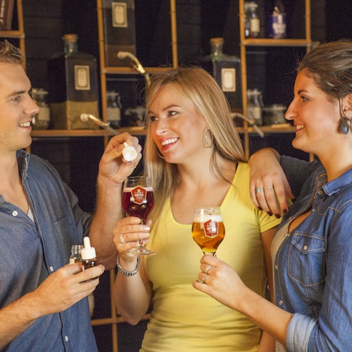 Három barát italokat élvez egy bárban, színes italokkal teli poharakat tartva, miközben a háttérben polcokon üvegek sorakoznak.