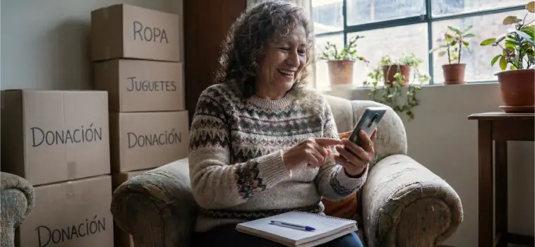 Mujer coordinando el recojo por WhatsApp junto a cajas de donación etiquetadas.