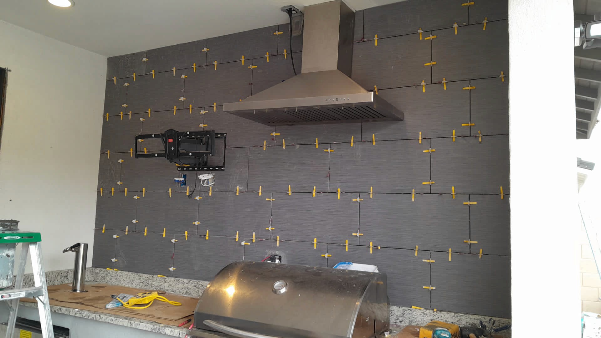 Modern kitchen with a stainless steel range hood and a dark tile backsplash under construction with spacers.