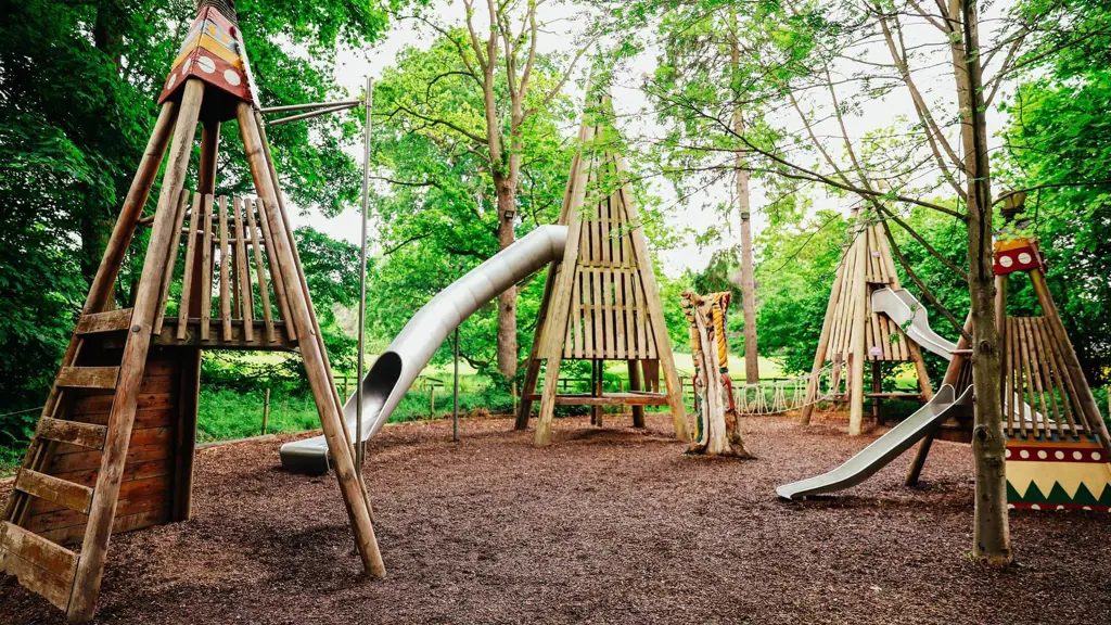 Natural wooden playground with teepee-shaped climbing structures and slides in forest setting