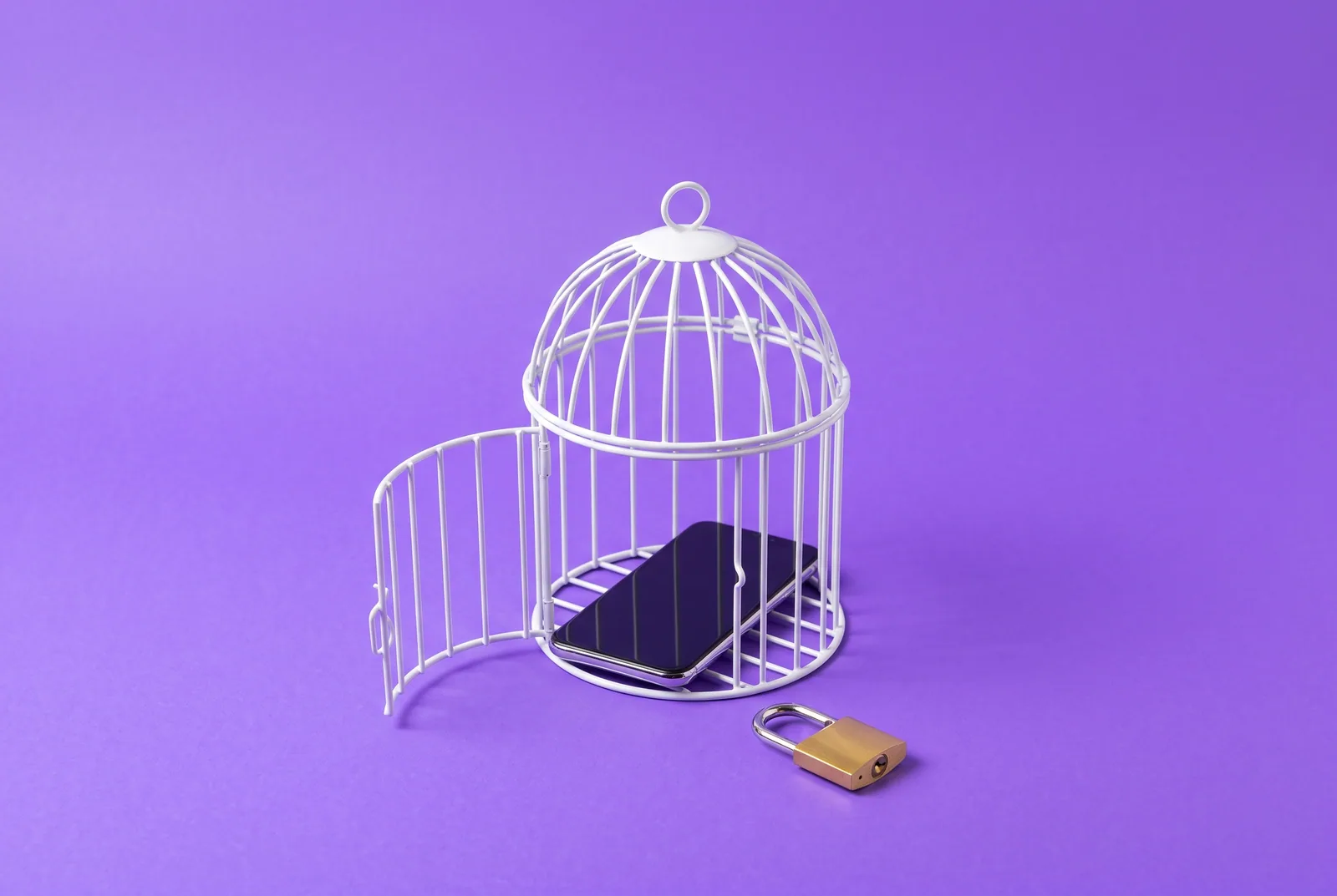 A plain smartphone resting inside a small open birdcage with a padlock beside it, a playful image for parental controls to block porn