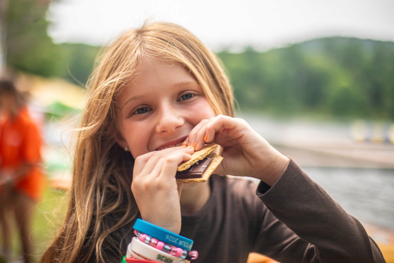 Camper eating a s'more at a Camp Lenox campfire