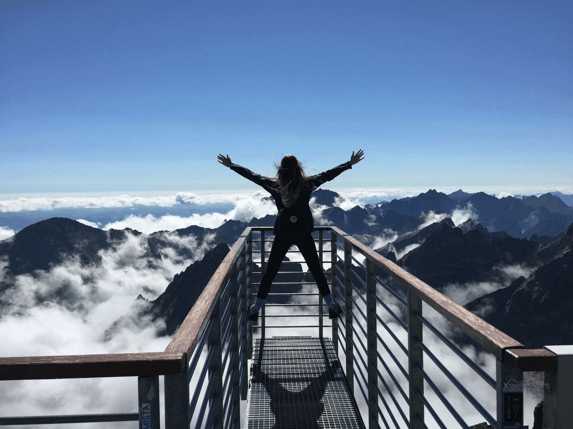 photo of woman at observation point overlooking mountains with hands raised