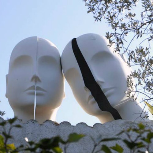 Two mannequin heads with split faces, one with a white stripe and the other with a black stripe, set against a blue sky and foliage.