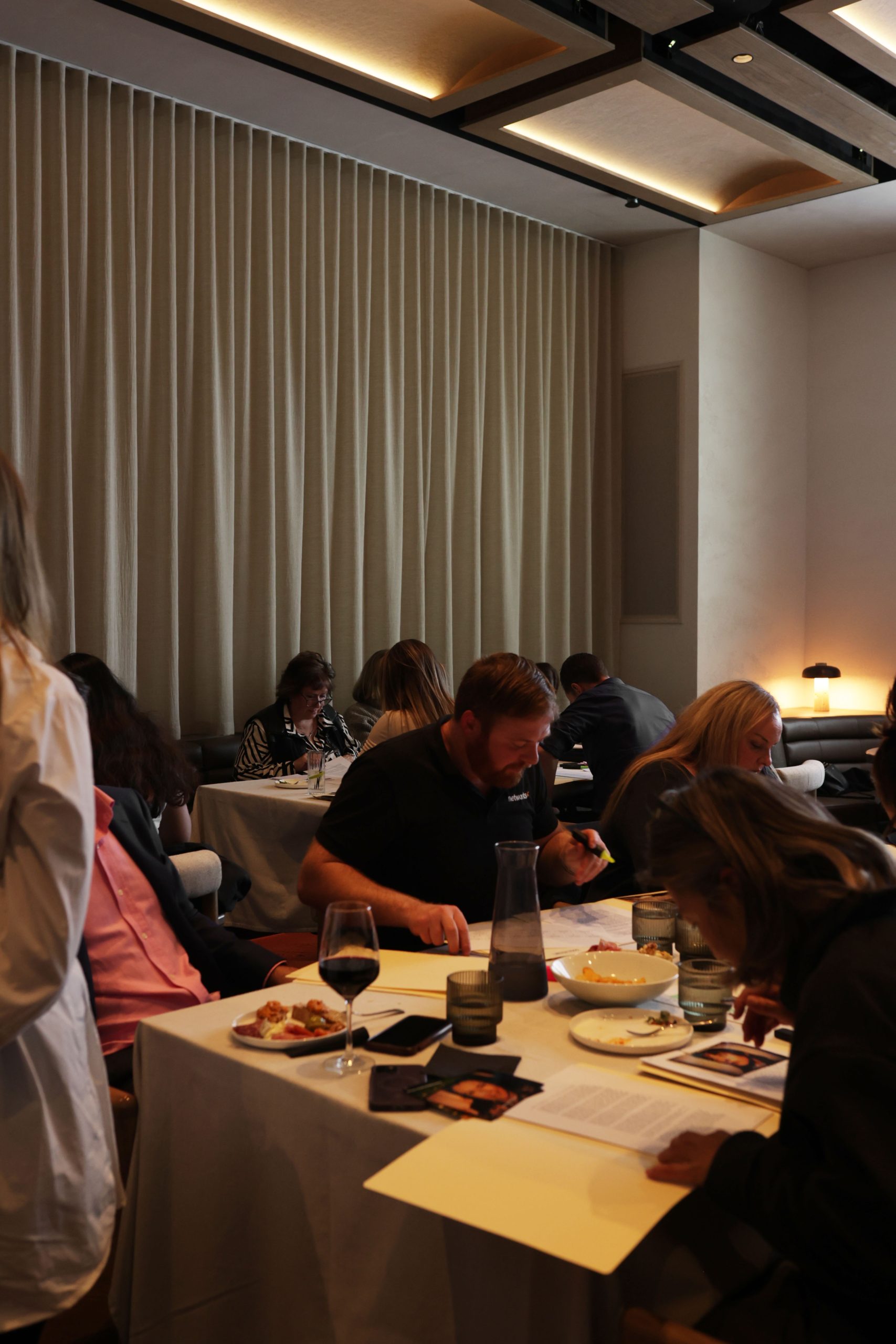 Guests seated at tables working through case file documents and photos, with wine and food set out