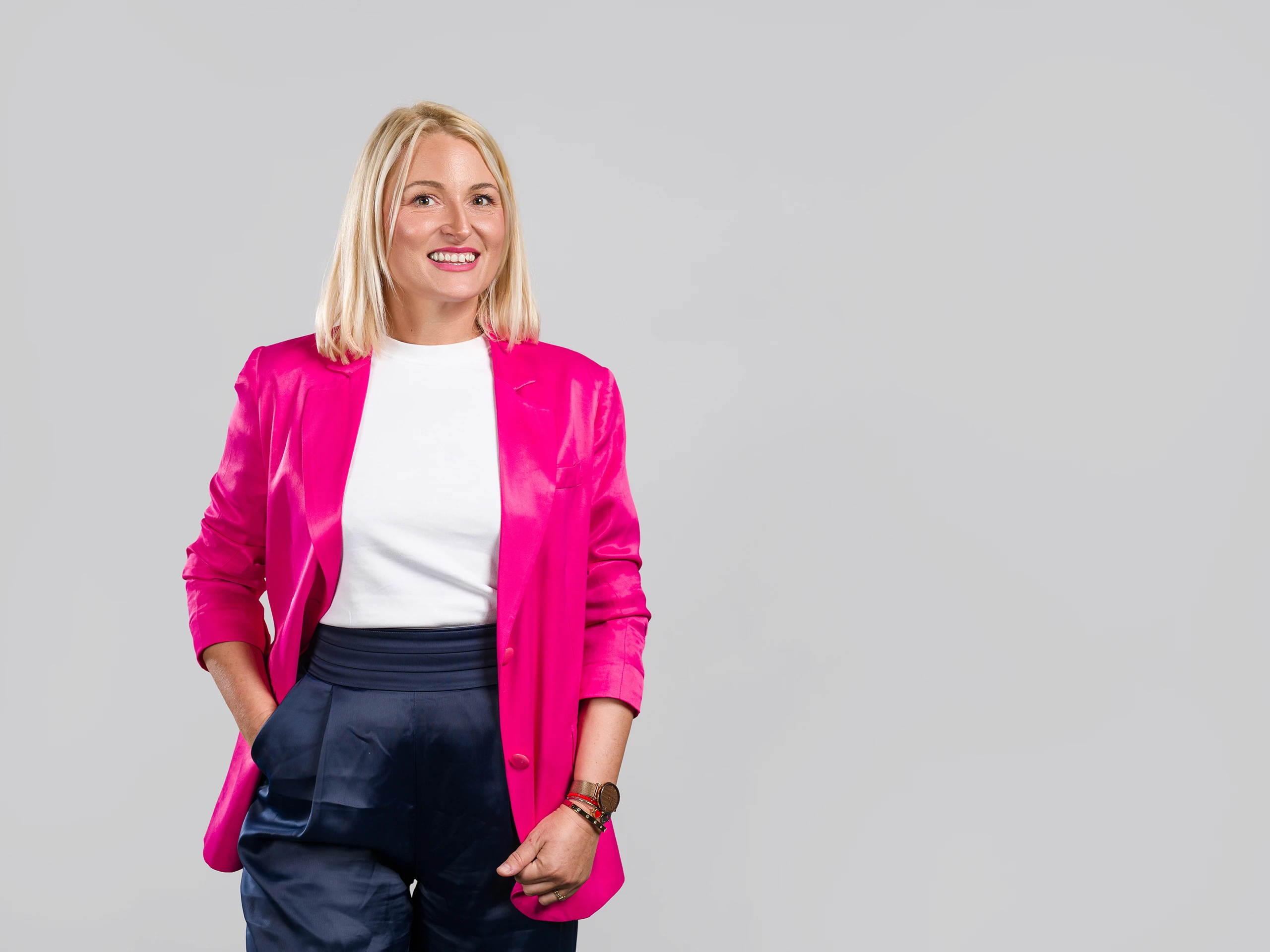 Corporate portrait of a confident woman in a pink blazer, photographed in a studio environment.