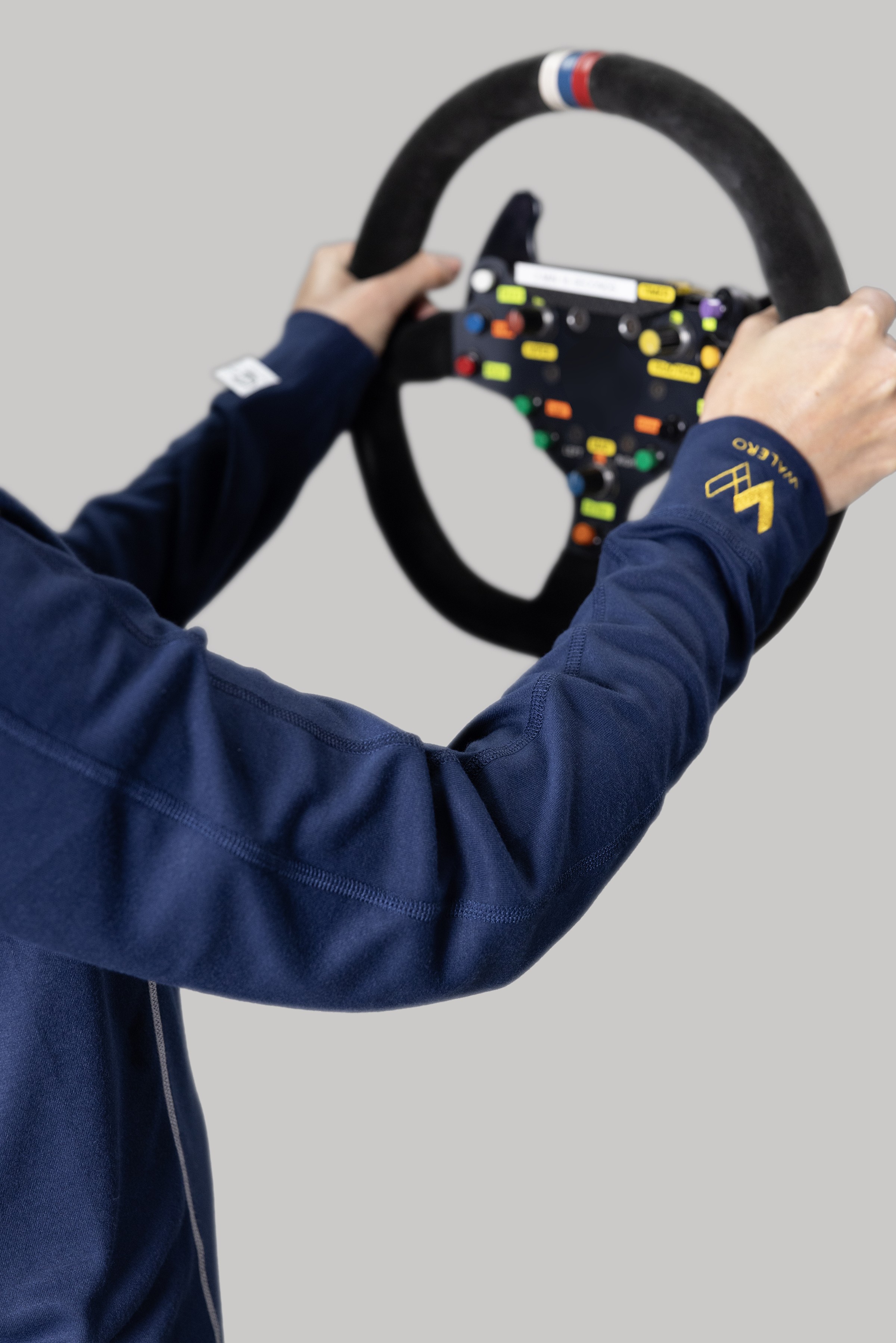 Driver in navy Walero base layer holding a racing steering wheel.