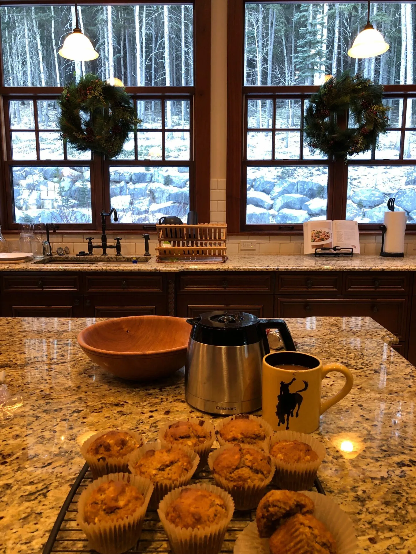 Image of freshly baked muffins in a large rustic kitchen with Christmas wreaths hanging on the window behind.