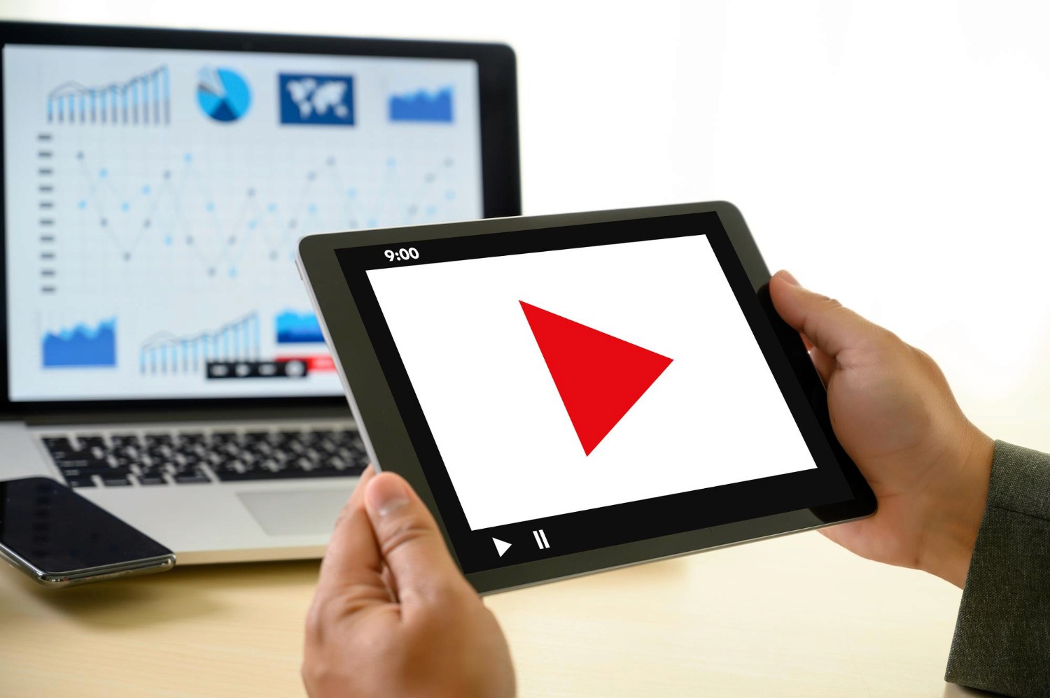 A person holding a tablet displaying a prominent red play button, indicating video playback or media selection.